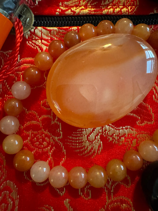 Amber colored bead bracelet and large polished amber stone on red and gold patterned fabric.