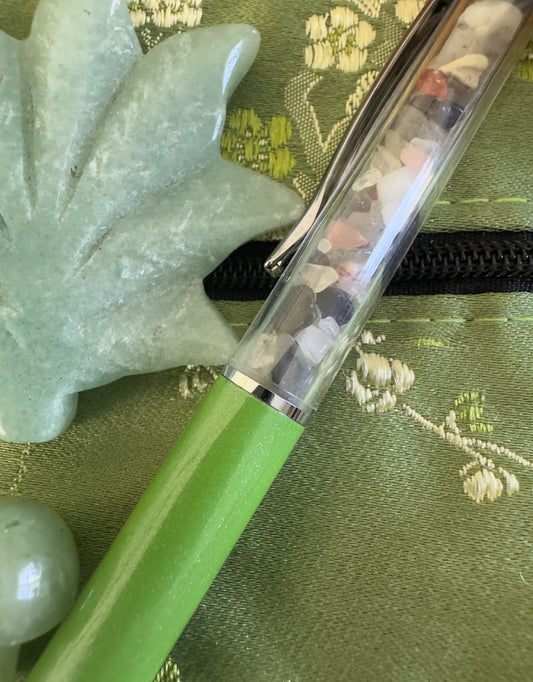 Green pen with colorful stones inside, green leaf, green background.