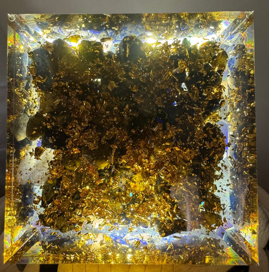 A transparent orgonite pyramid featuring a tightly wound copper spiral embedded in the center, with shimmering metal filings scattered throughout