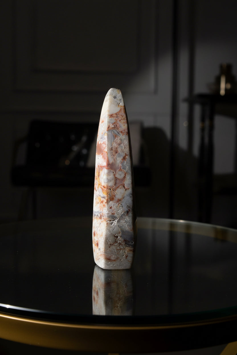 sideview of a crazy lace agate freeform colors are brown, tan, off white freeform is place on a glass top table