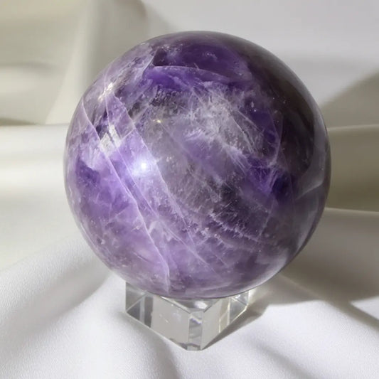close up amethyst sphere with obvious iron inclusions - Likely hematite and natural fractures purples and white colors white fabric backdrop