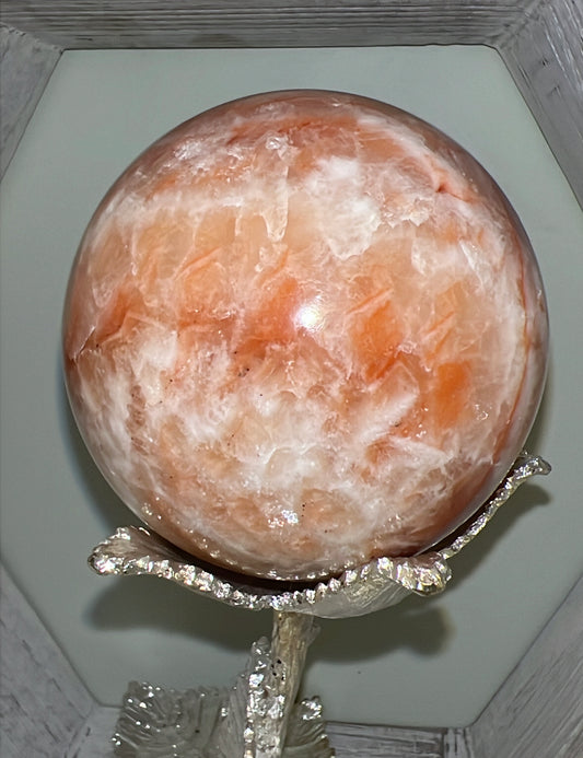 An orange and white crystal ball on a silver, floral-shaped stand.