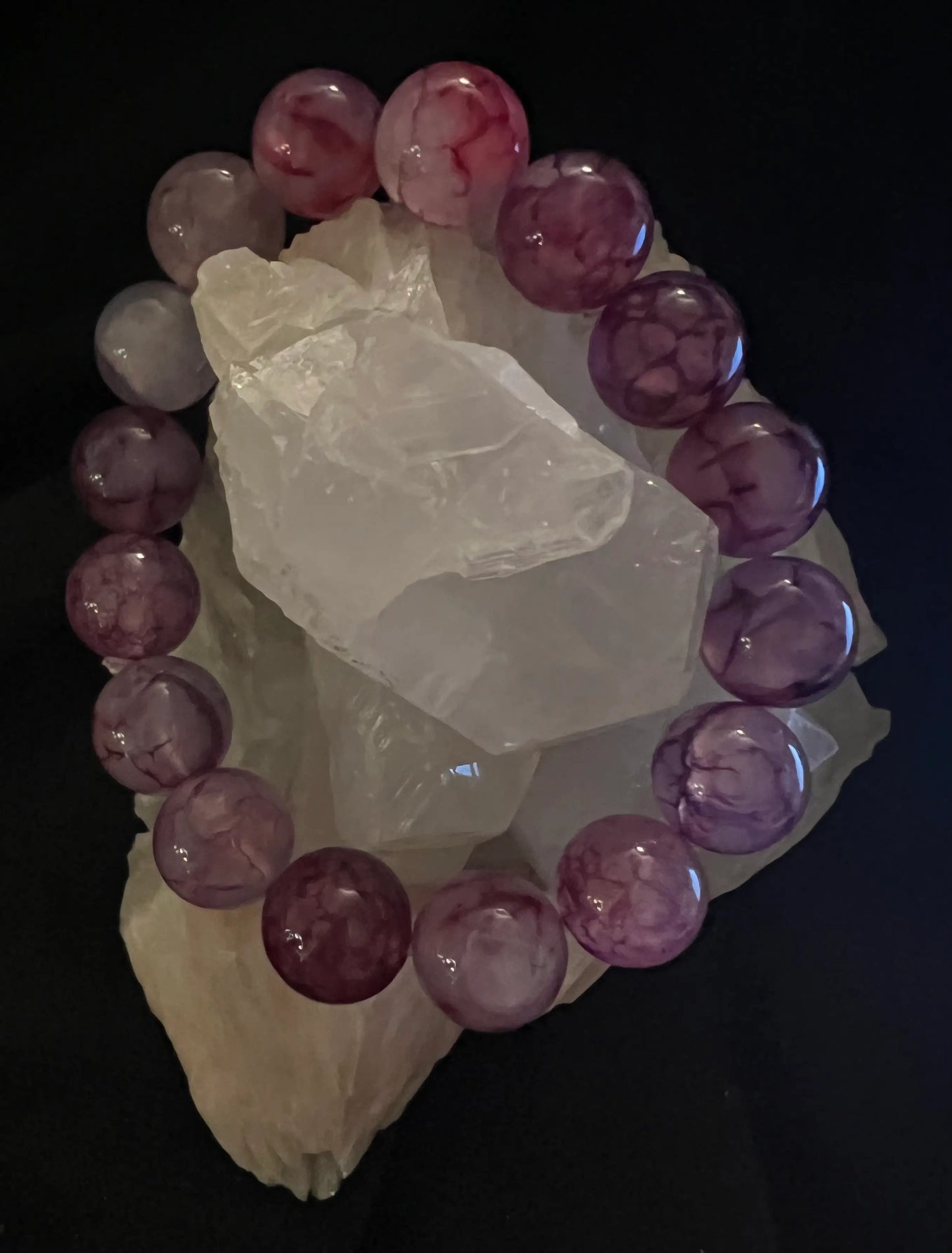 Purple beaded bracelet encircling a cluster of clear crystals on a black background.