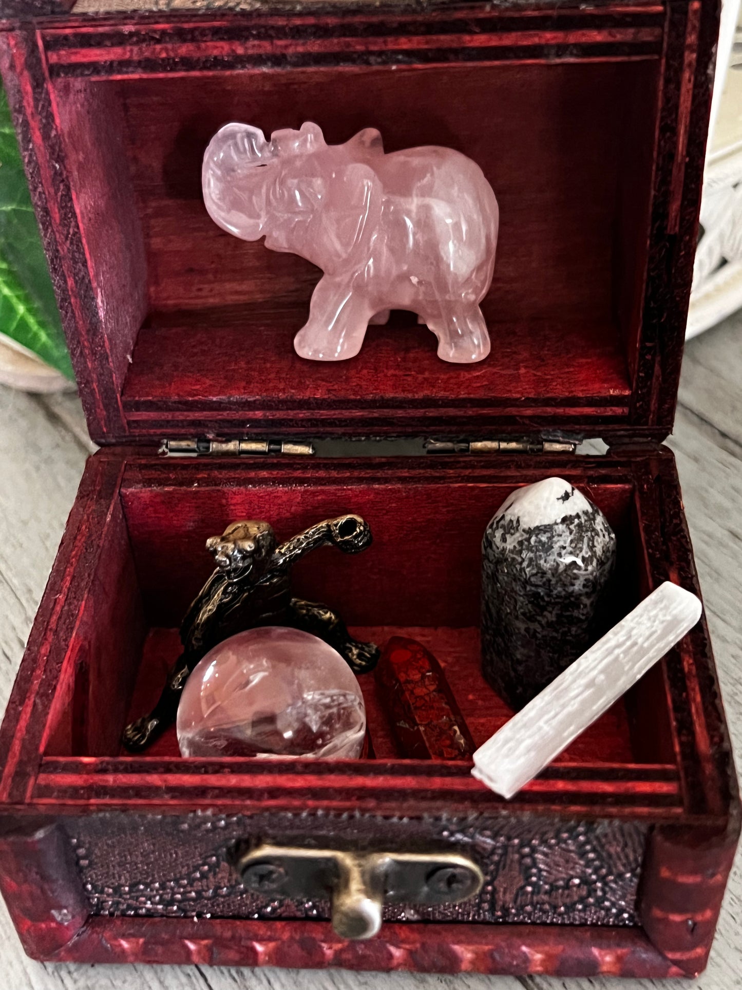 Open red wooden box with rose quartz elephant, metal turtle, quartz ball, red crystal, and white selenite.