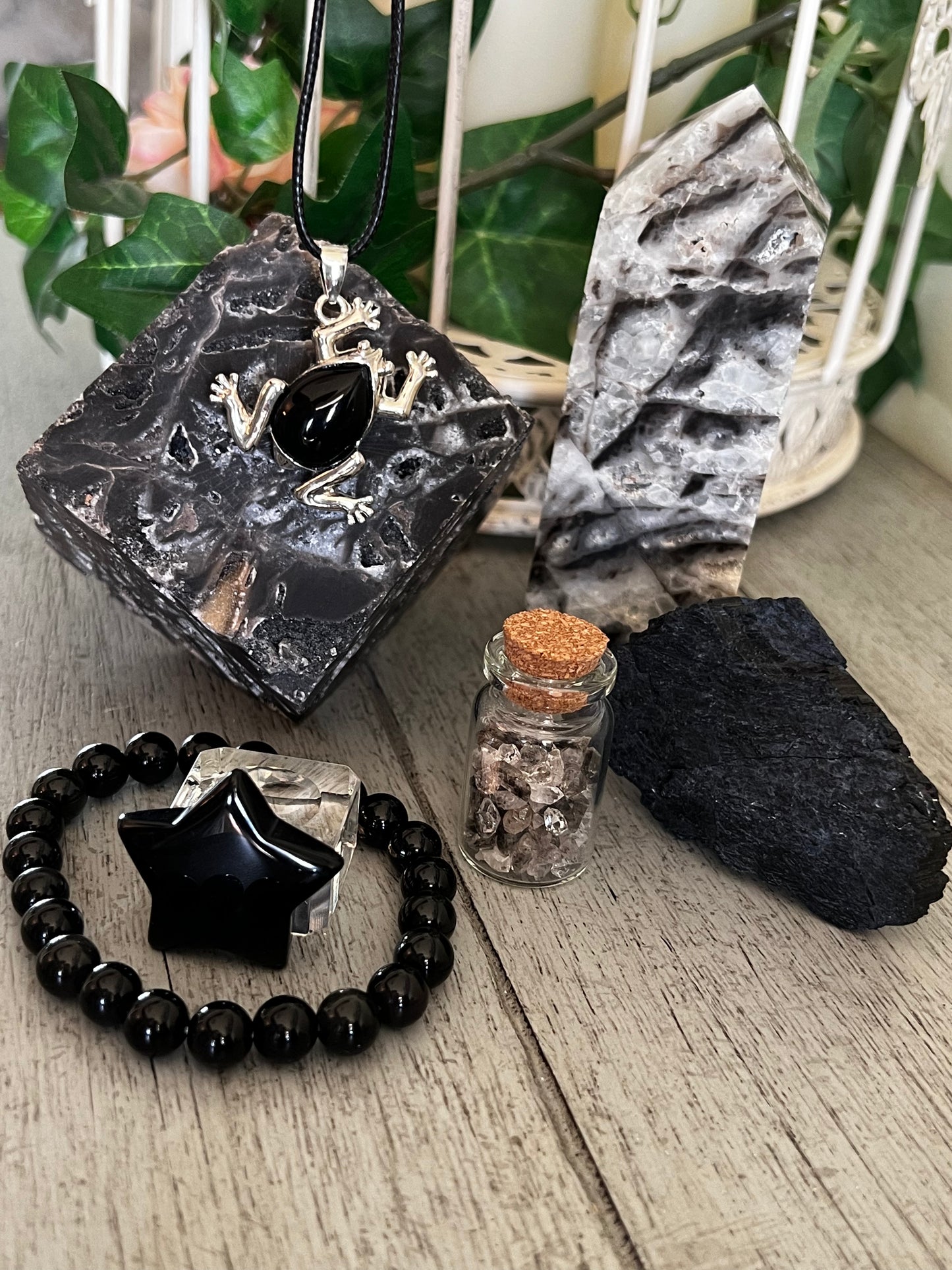 Arrangement of black and grey crystals, a black star bracelet, and a silver frog pendant on a wood surface.