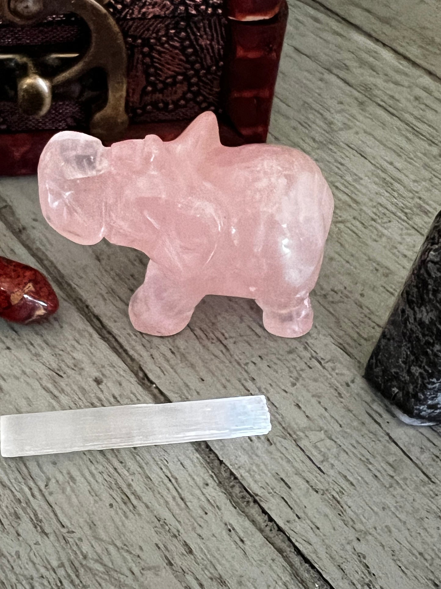 Close-up of a pink crystal elephant, a red stone, a white crystal bar, and a black stone on a gray wooden surface.