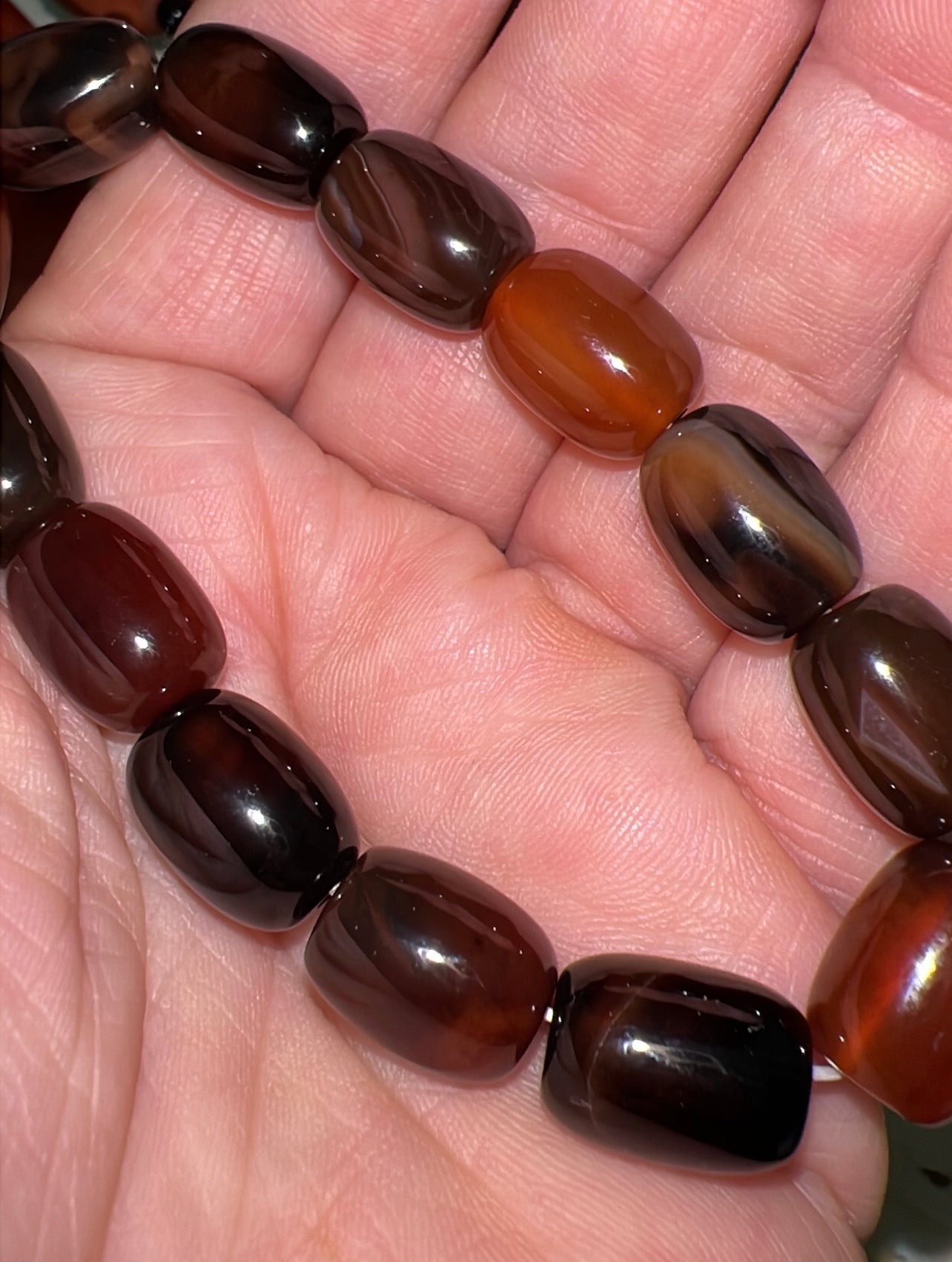 Close-up of a hand holding a beaded bracelet of brown and orange polished stones.