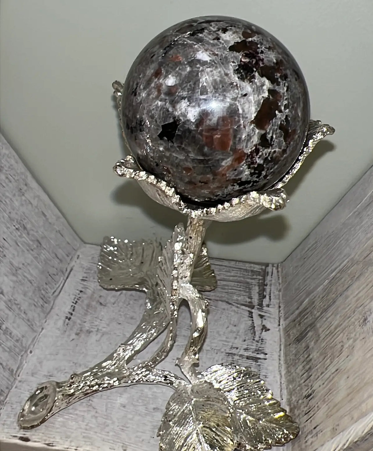 Gray and brown sphere held in silver floral stand.