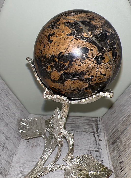 Brown and black patterned sphere atop a silver, jewel-encrusted floral stand.