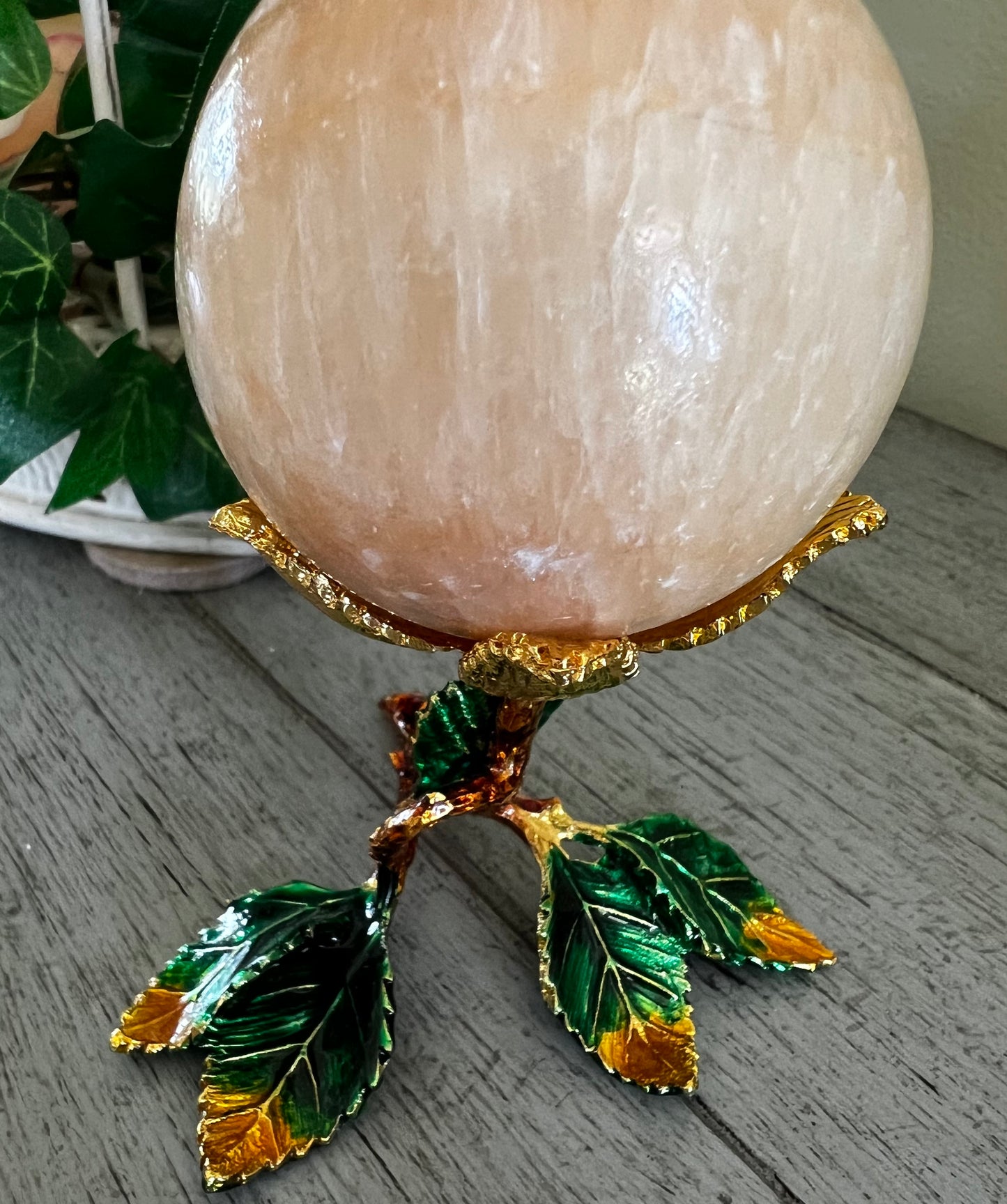 Peach-colored stone sphere on a gold and green leaf stand.