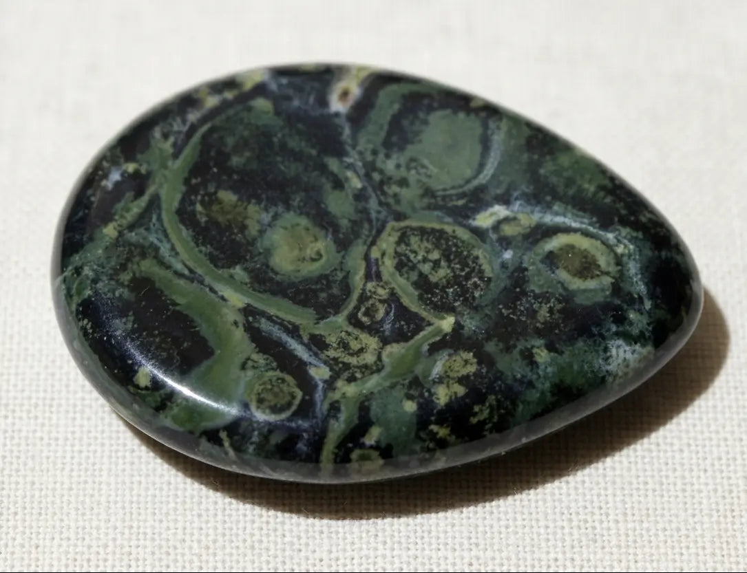 close up of kambaba jasper worry stone bright hues of greens, with black swirls