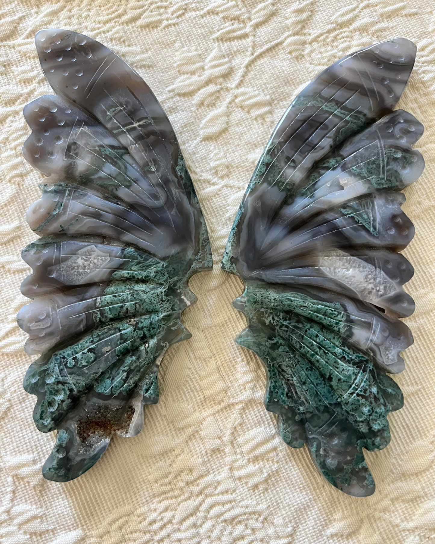Two carved agate butterfly wings on a textured white surface.