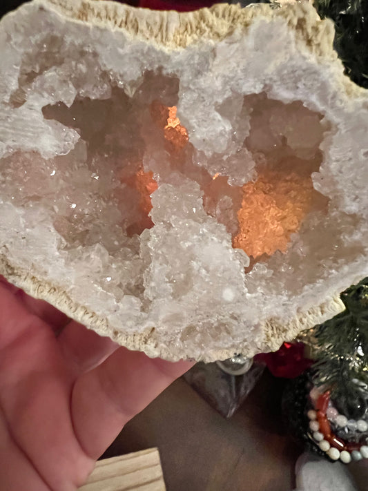 Close-up of a crystal geode with light brown outer shell and clear crystals inside, held in a hand.
