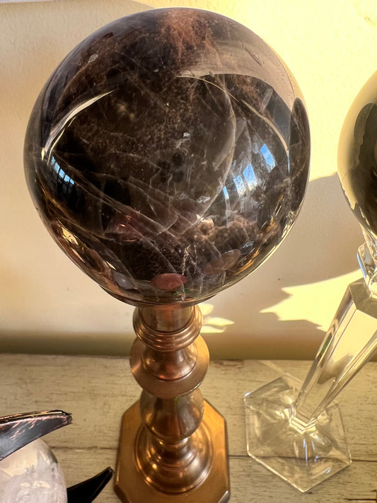 A dark brown crystal ball rests on a gold metal stand.