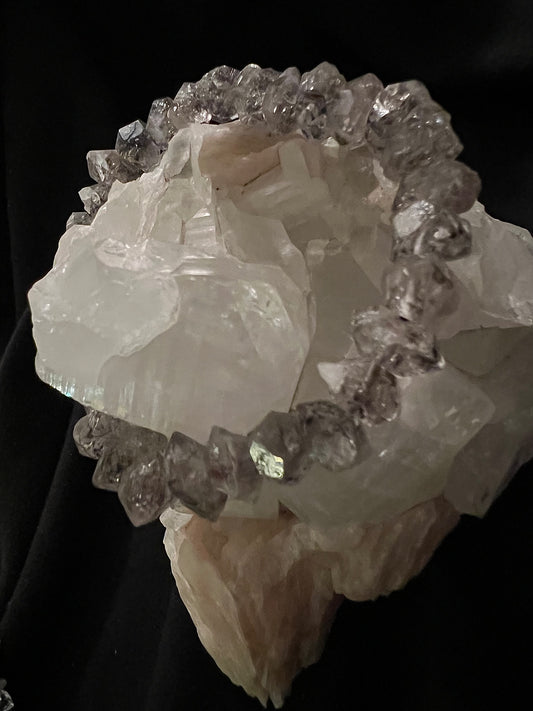 Clear calcite formation with a dark crystal bead bracelet.