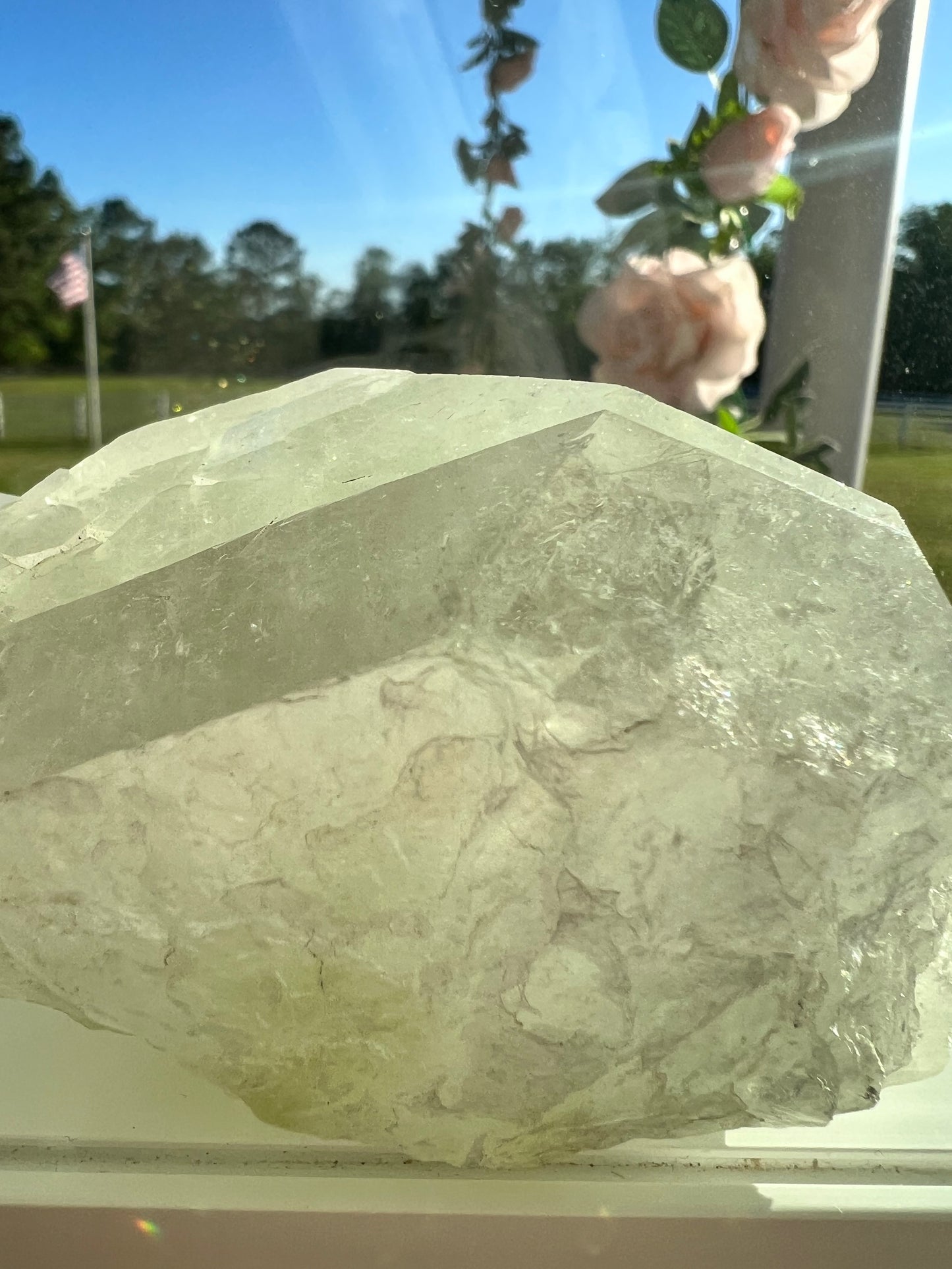 Large light green crystal on a windowsill. Outside, pink roses and an American flag are visible.