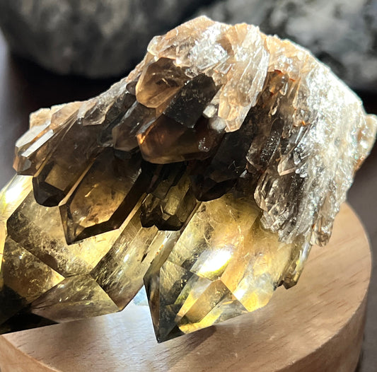 Close-up of a cluster of brown and clear quartz crystals on a wooden stand.
