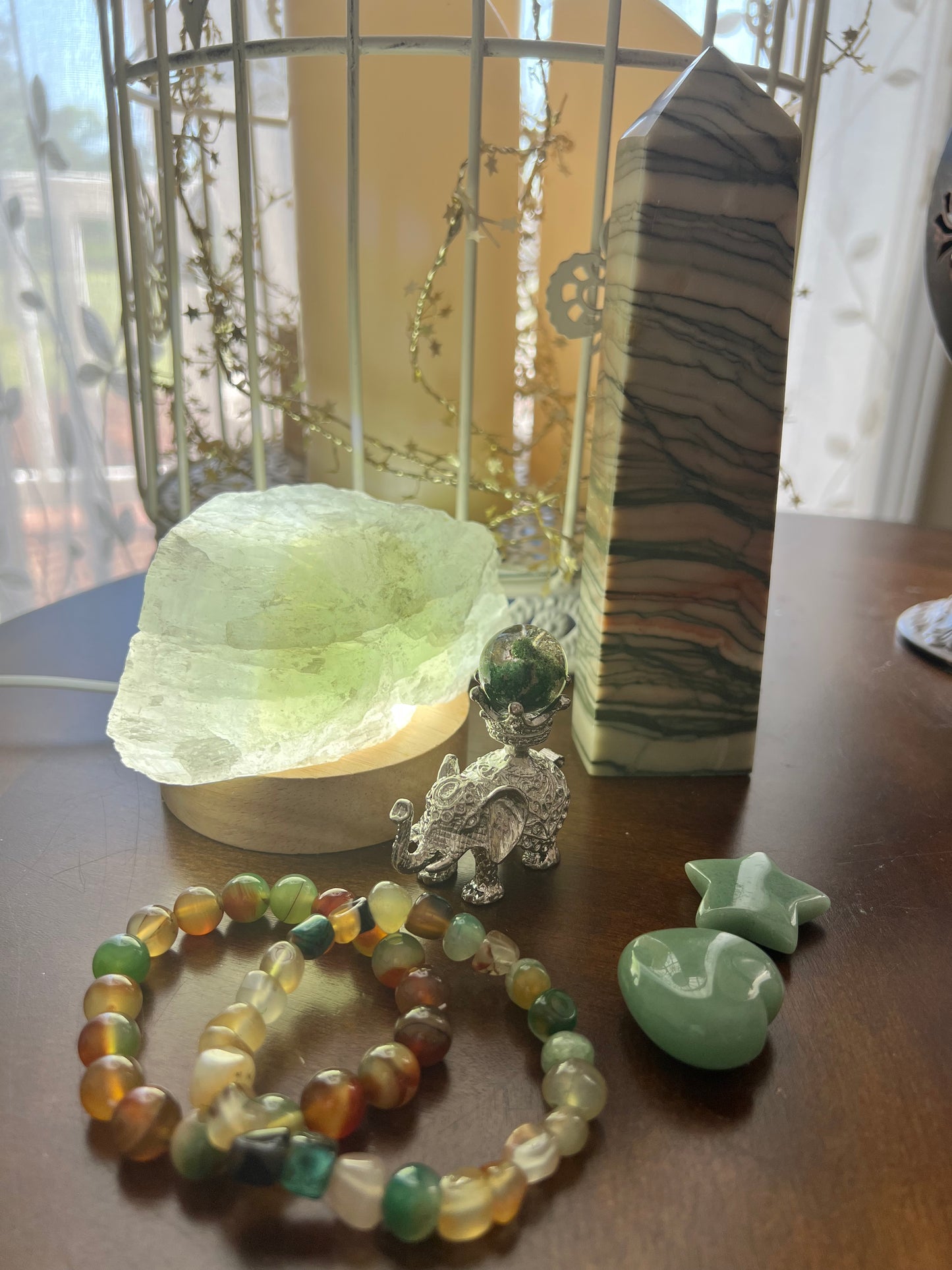 A still life with crystals, a decorative elephant figurine, and beaded bracelets on a wooden surface.