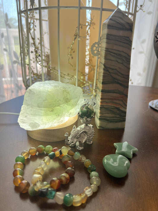 A still life with crystals, a decorative elephant figurine, and beaded bracelets on a wooden surface.
