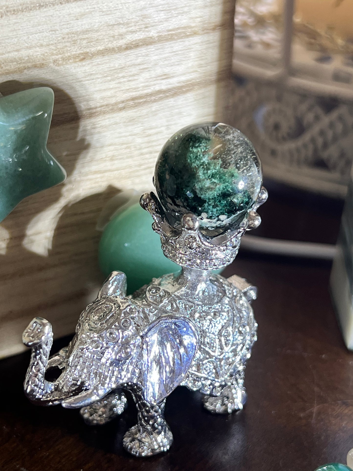 Silver elephant figurine holding a green sphere.