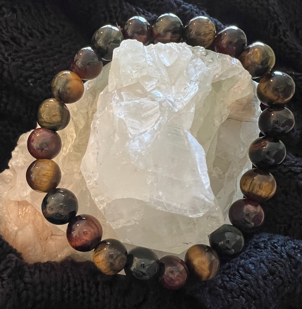 Bracelet made of brown, red, and black stone beads, wrapped around a clear crystal on a dark knit background.