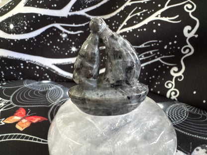Gray stone carving of embracing figures on a clear crystal base.