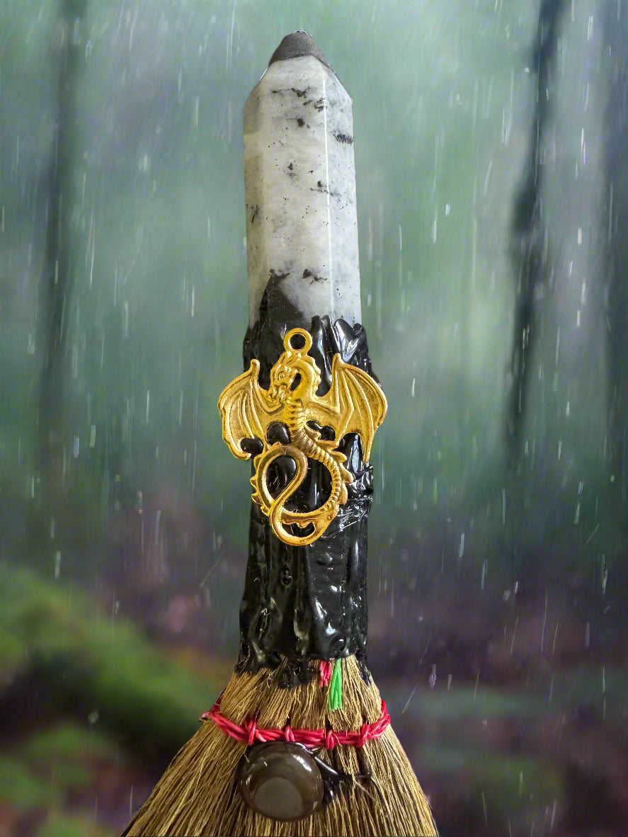 Broom with white crystal tip, gold dragon charm, and rain background.