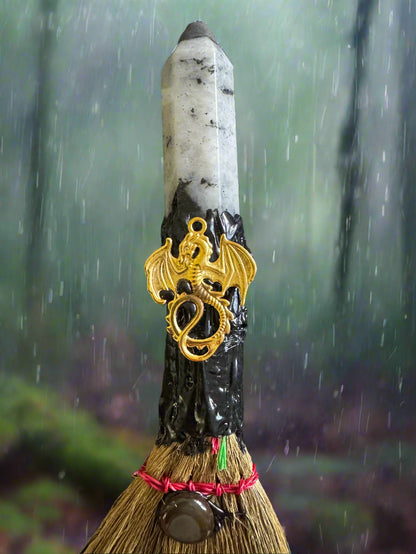 Broom with white crystal tip, gold dragon charm, and rain background.