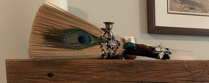 Hand crafted besom / altar broom clear quartz finial natural bristles silver bee charm and rare peacock feather  on a fireplace mantle