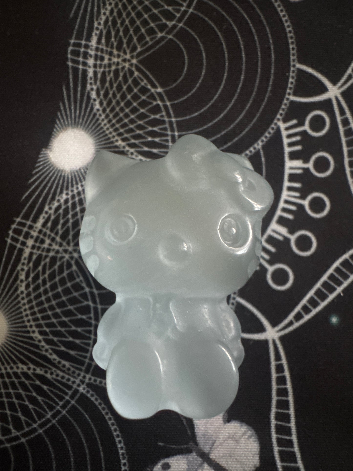 A pale blue Hello Kitty figurine on a black surface with white geometric designs.