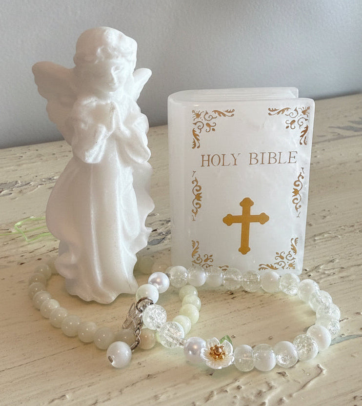 White Calcite Carving Angel with two white crystal bead bracelets. next to the angel is a carving of the holy bible with gold text and a gold cross quartz crystal
