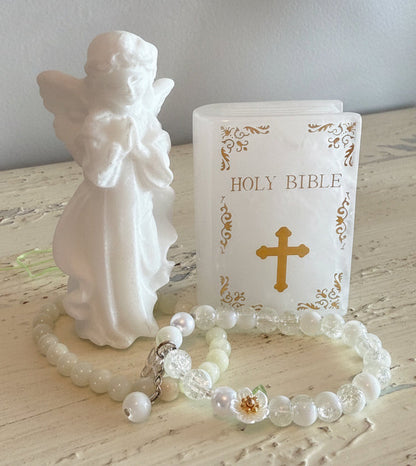 White Calcite Carving Angel with two white crystal bead bracelets. next to the angel is a carving of the holy bible with gold text and a gold cross quartz crystal