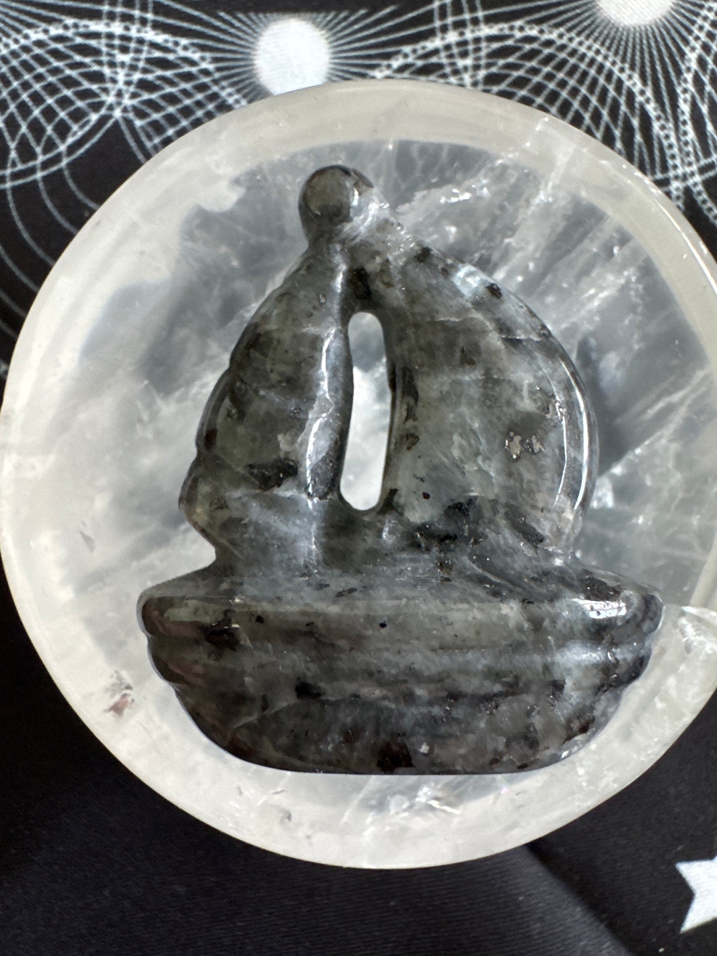Close-up of a gray stone sculpture with a vertical slit, nestled in a clear quartz bowl on a patterned fabric.
