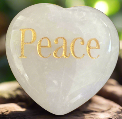 Close-up of a white, heart-shaped stone inscribed with the golden word "Peace".