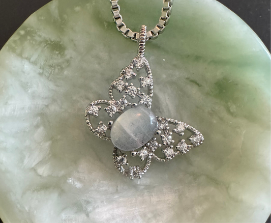 A butterfly pendant necklace made of sterling silver and a grey cabochon. The wings are adorned with white stones.
