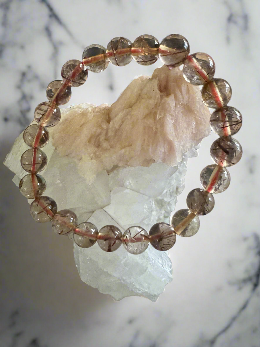 Bracelet of round clear beads with red and black inclusions, displayed on white crystal.
