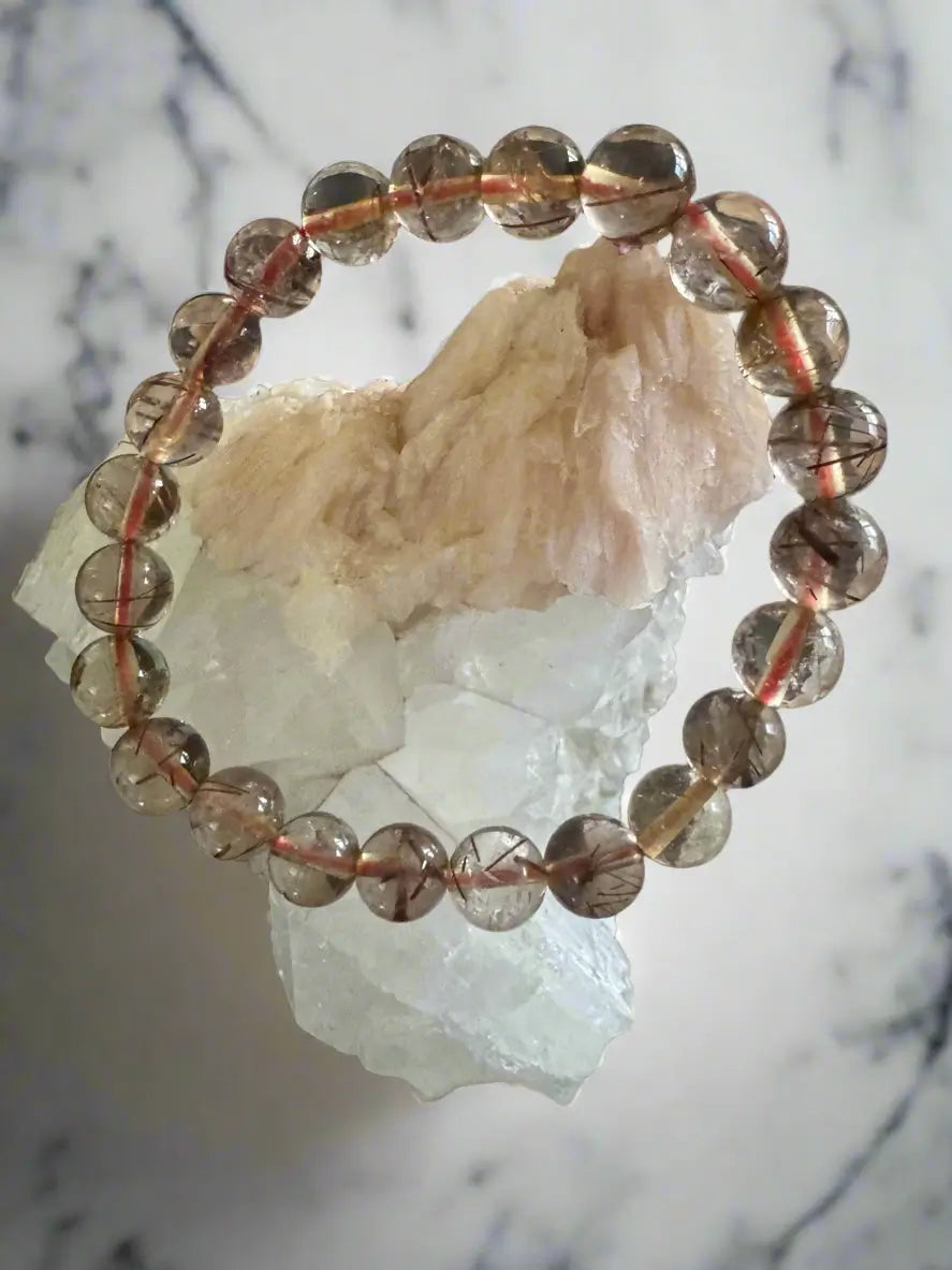 Bracelet of round clear beads with red and black inclusions, displayed on white crystal.
