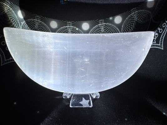 Selenite crescent bowl on a clear stand with a star pattern, resting on a black patterned cloth.