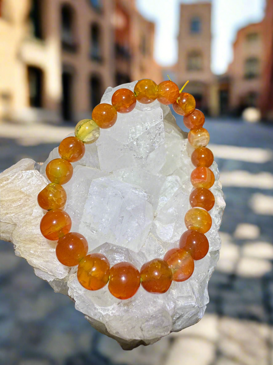 Orange beaded bracelet on a clear crystal rock against a blurred outdoor backdrop.