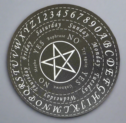 Close-up of a black and white talking board with a star in the center and letters, numbers, and days of the week around the edge.