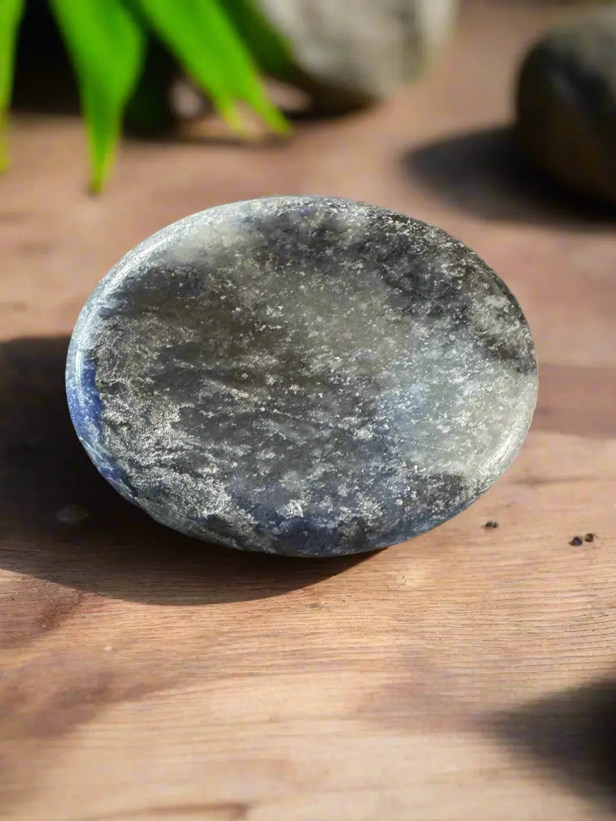 Polished, round, grey and blue labradorite stone on wooden surface.