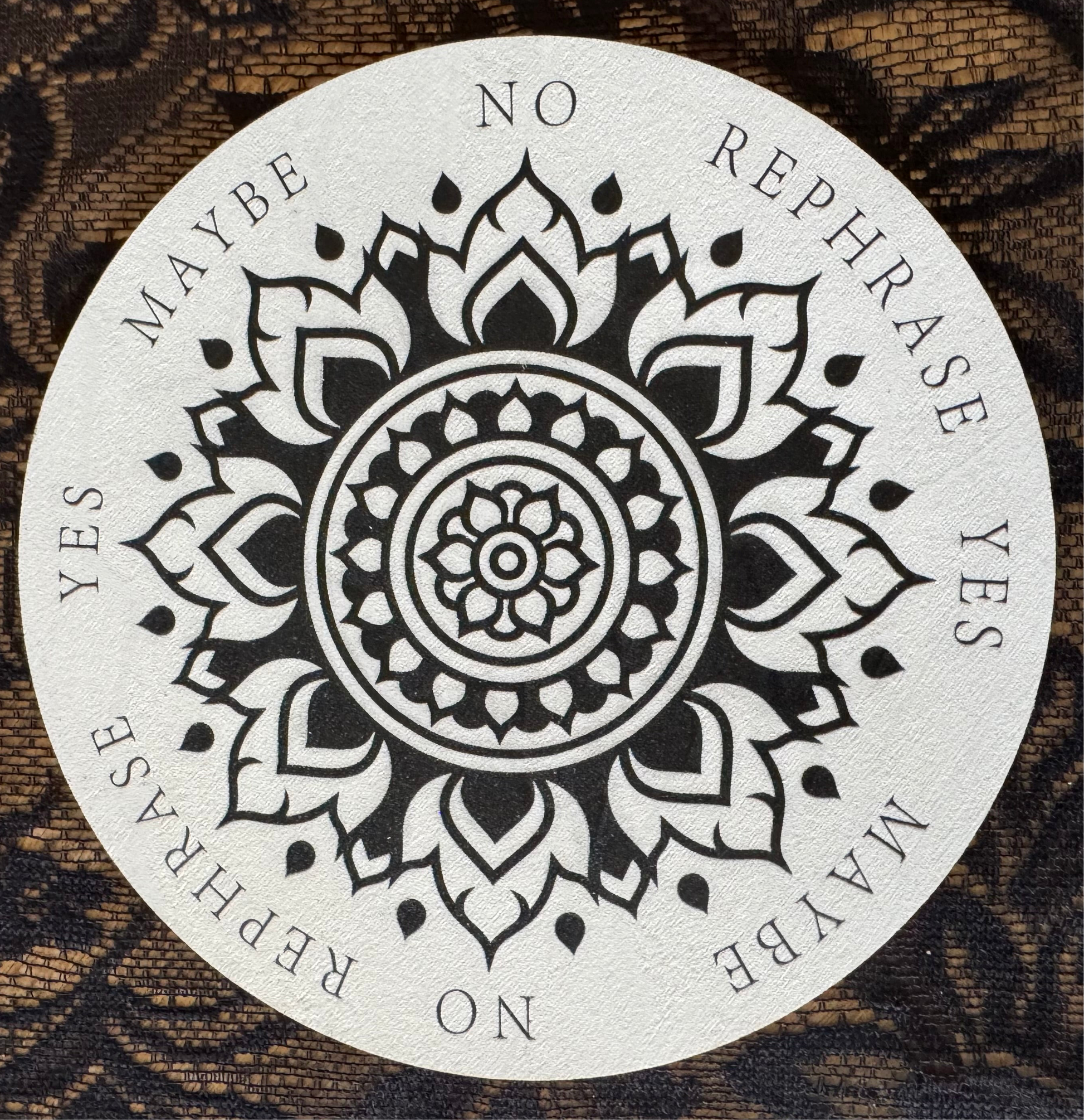 Circular divination board with floral mandala design. "Yes," "No," "Maybe," and "Rephrase" options. Lace background.
