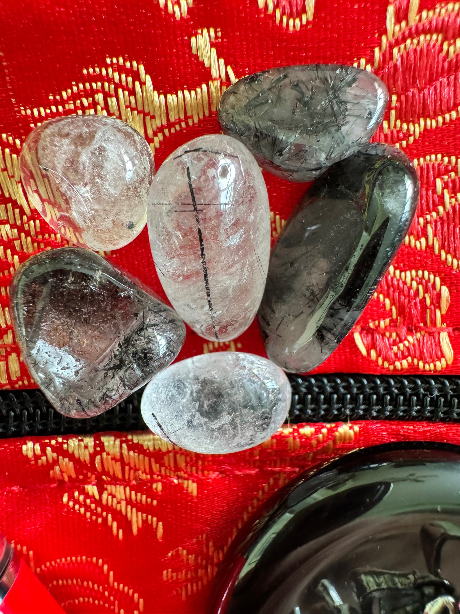 Six tumbled black tourmalinated quartz stones on a red and gold patterned fabric.