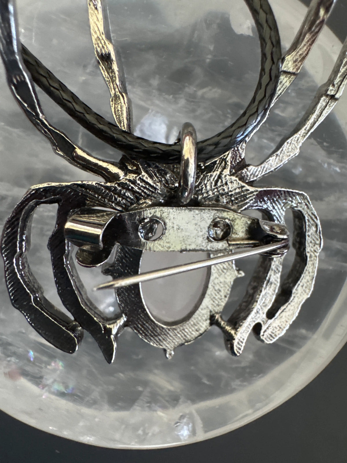 Back of a silver spider brooch with a light pink stone.