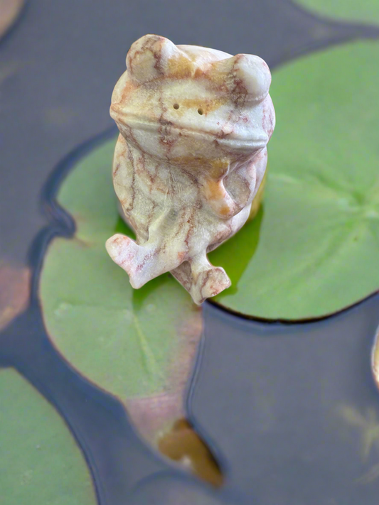 Stone frog figurine sits on a lily pad.