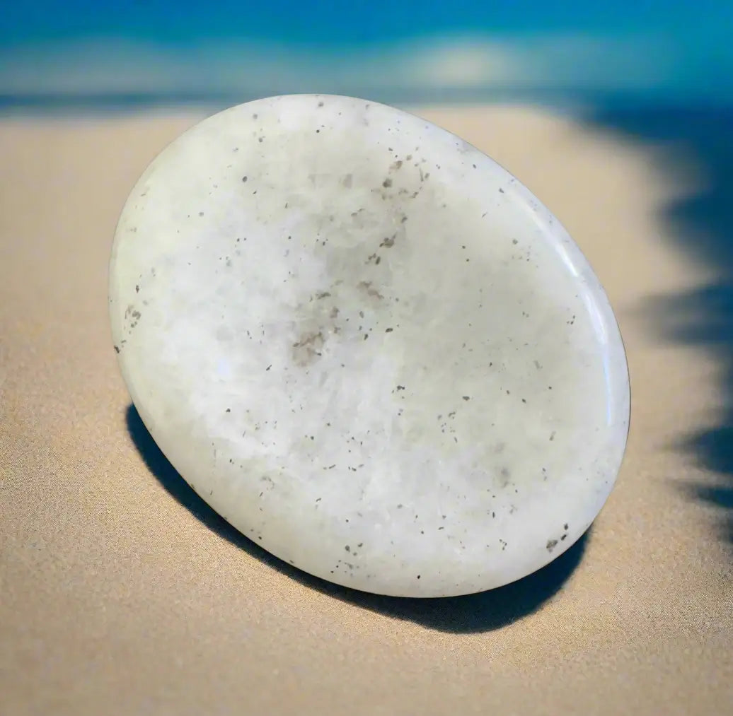 Oval white stone with dark specks on a tan beach background.
