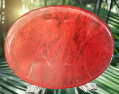 Close-up of a polished, red stone disc on a clear plastic stand.