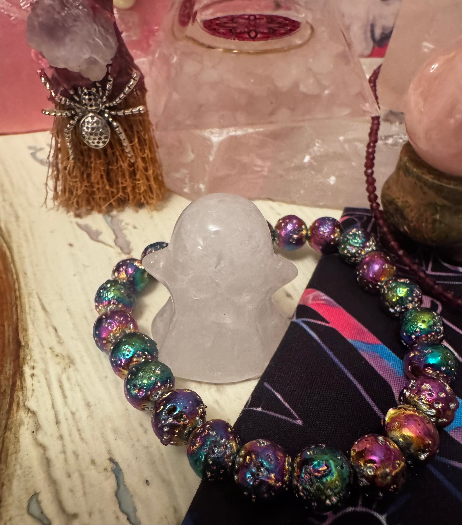 A collection of crystal objects including a ghost-shaped crystal, a colorful beaded bracelet, a rose quartz sphere, and a spider-topped broomstick.