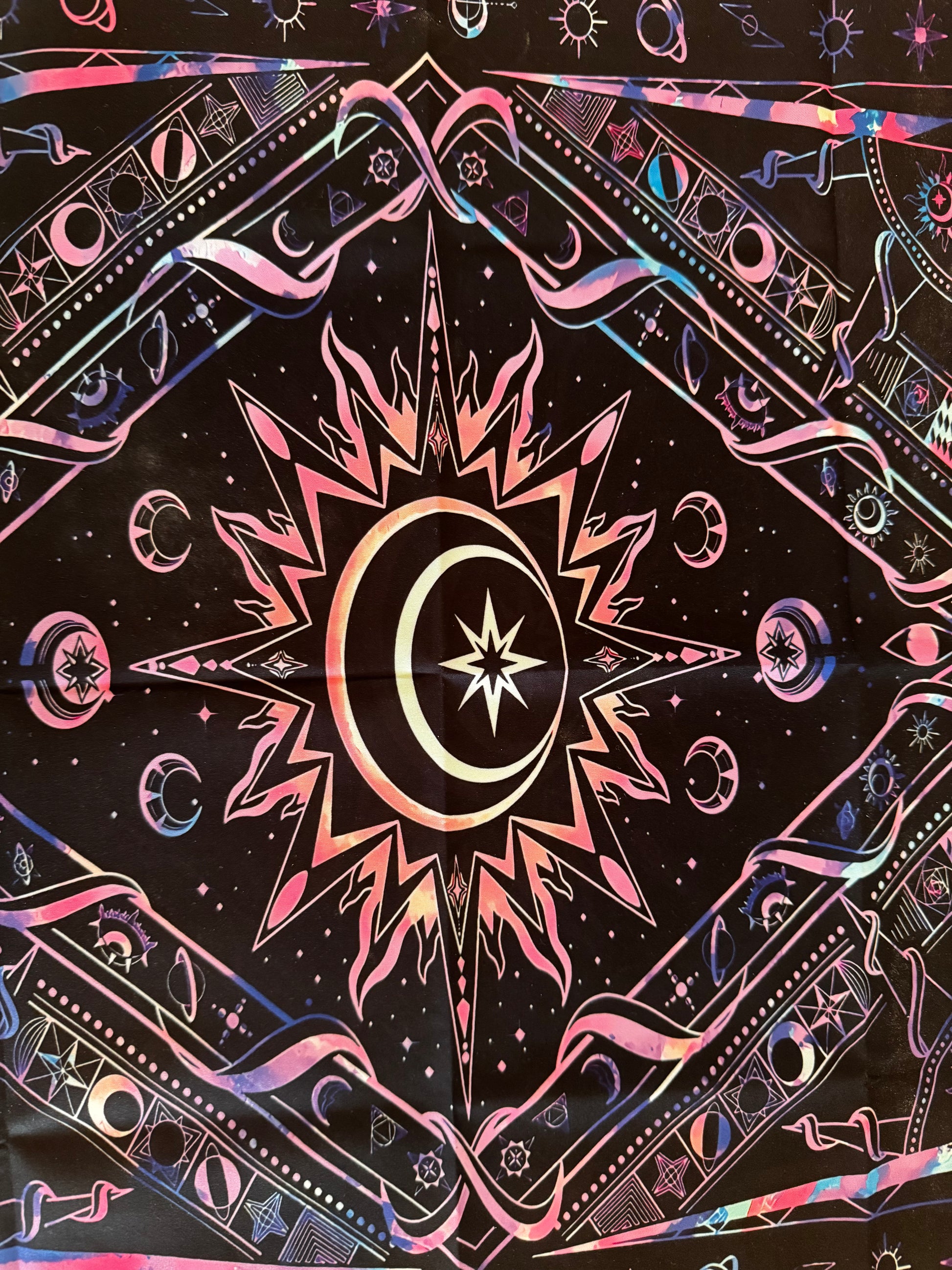 Mystical patterned fabric tapestry with central sun, moon, and star motif in pink, blue, and white on black.