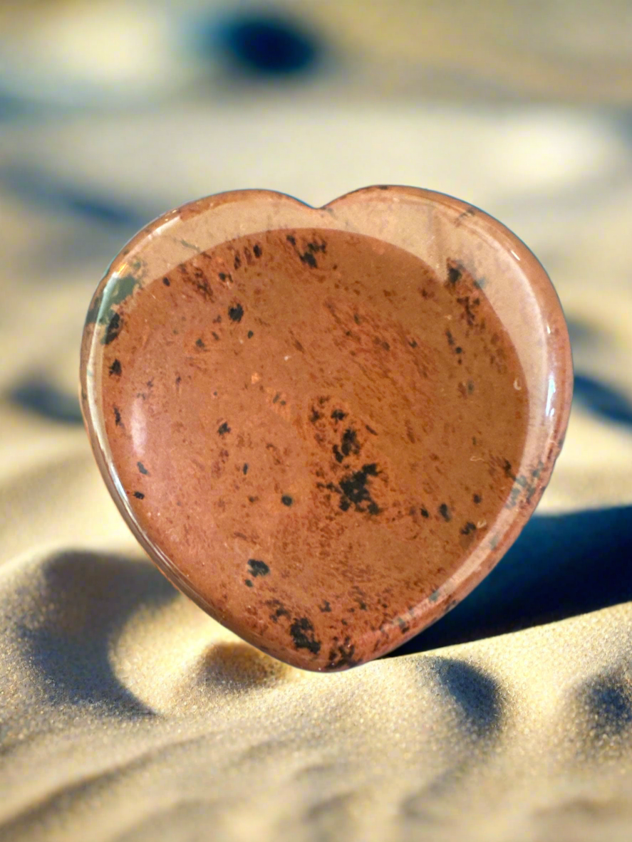 Close-up of a heart-shaped, brown and black speckled stone on sand.